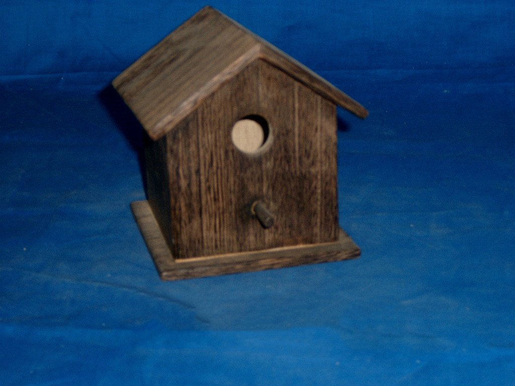 Simple driftwood-stained wooden bird house with pitched roof, round entrance and perch
